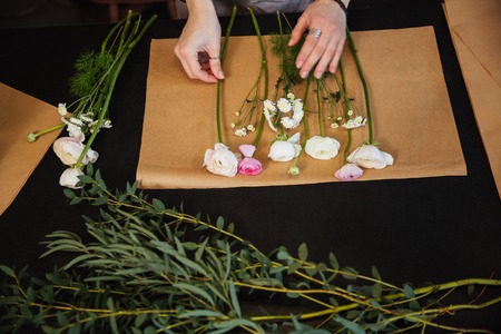 Top view of hands of young woman florist choosing flowers and making boquet on black tableの写真素材