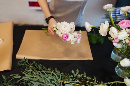 Top view of hands of female florist holding flowers for creating bouquet on black table