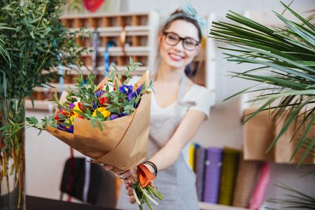 Happy charming young woman florist giving bouquet of colorful flowers to youの写真素材