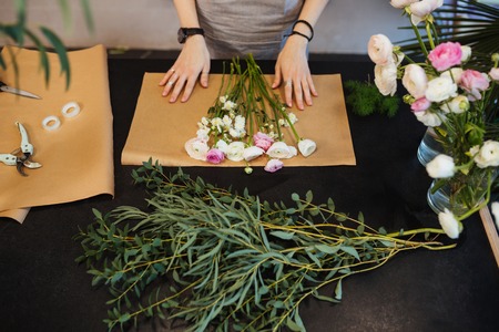 Top view of hands of female florist designing and creating flower bouquet on black table
