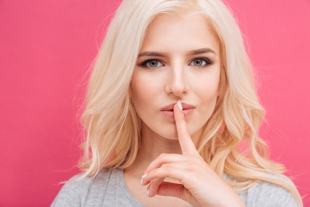 Pretty woman showing finger over lips on pink backgroundの写真素材