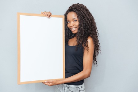 Smiling afro american woman showing blank board over gray background