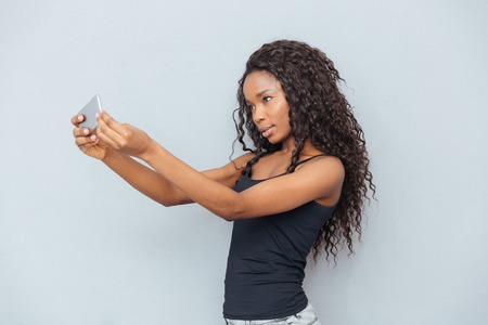 Afro american woman making selfie photo on smartphone over gray backgroundの写真素材