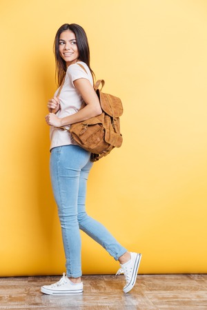Full length portrait of a charming woman with backpack posing on yellow backgroundの写真素材
