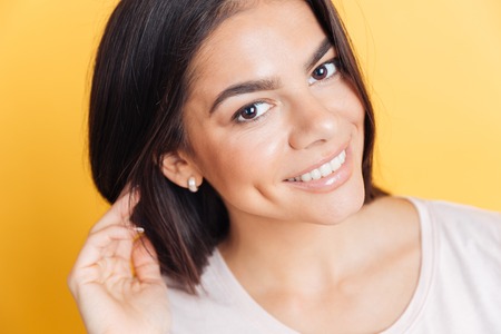 Closeup portrait of a smiling lovely woman looking at camera over yellow backgroundの写真素材