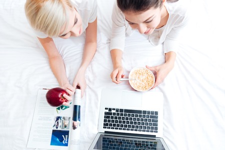 Top view portrait of a two women lying on the bed and using laptop computerの写真素材