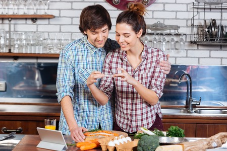 Smiling young couple cooking and taking photos with smartphone on the kitchenの写真素材
