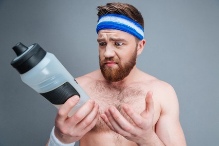 Portrait of sad upset young sportsman with empty bottle for water over grey backgroundの写真素材