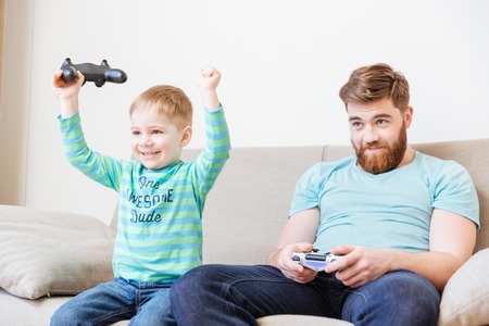 Cheerful excited little son playing computer games with father and winning
