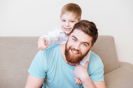 Portrait of happy father and son sitting on sofa at home togetherの写真素材