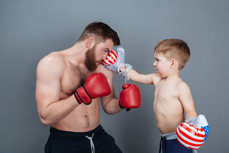 Dad and son playing using boxing gloves together over grey backgroundの写真素材
