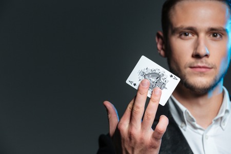 Portrait of handsome young magician holding ace card over grey background