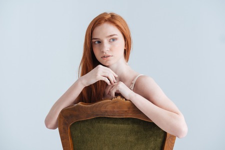 Pensive redhead woman sitting on the chair and looking away isolated on a white backgroundの写真素材