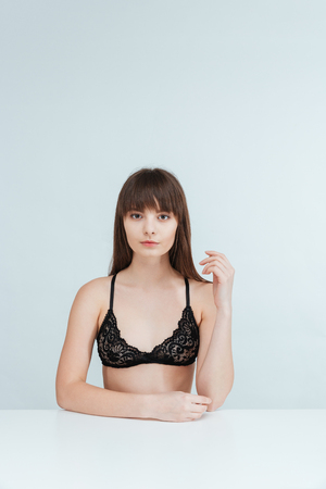 Charming woman in lingerie sitting at the table isolated on a white background and looking at cameraの写真素材