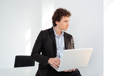 Pensive businessman leaning on the table with laptop computer and looking away