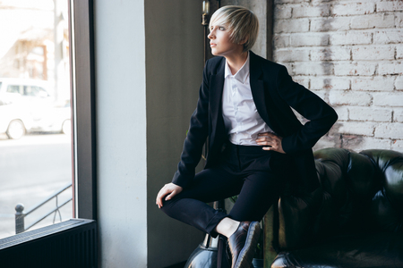 Beautiful blonde stylish girl sitting in a cafe and looking in the windowの写真素材