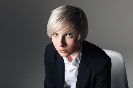 Serious stylish woman sitting on the chair over gray background and looking at cameraの写真素材