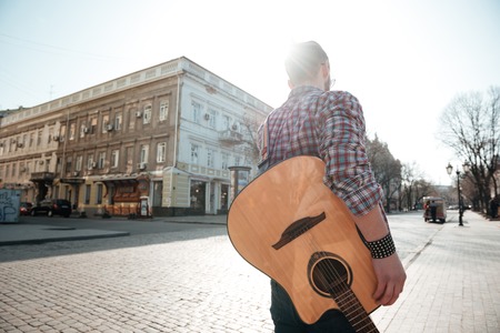Back view portrait of a man walking with guitar outdoorsの写真素材