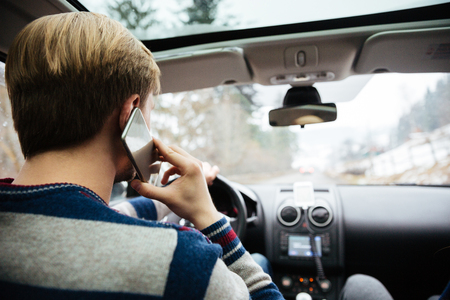 Back view of young man in striped sweater driving and talking on mobile phoneの写真素材