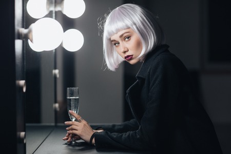 Portrait of attractive blonde young woman with glass of champaigne in dressing roomの写真素材