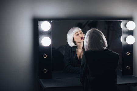 Seductive blonde young woman drinking champagne and looking at the mirror in dressing roomの写真素材