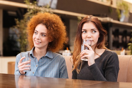 Two pretty young women sitting in cafe and drinking waterの写真素材