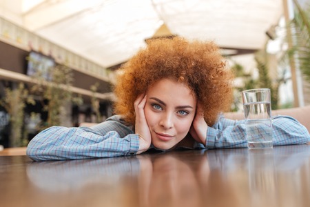 Attractive curly young woman with glass of water sitting and relaxing in cafe