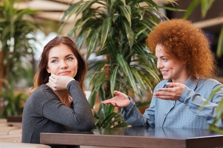Happy and sad young women sitting and talking in cafeの写真素材