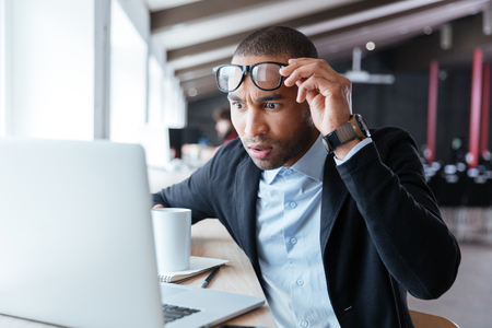 Businessman receiving negative news, touching his glasses, being mad, upset and surprised in front of laptopの写真素材
