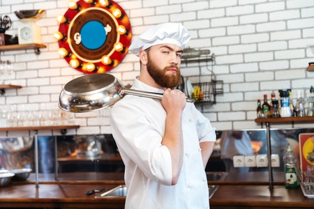 Serious attractive chef cook standing and holding frying pan on the kitchenの写真素材