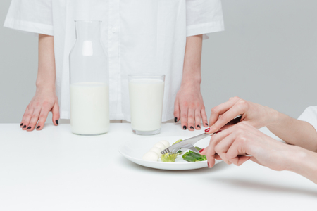 Close-up of hands holding knife and fork over vegetable salad during lunch over gray backgroundの写真素材