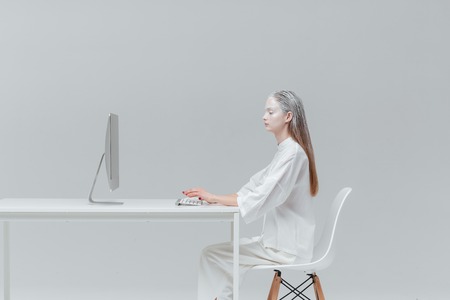Cosmic fashion woman sitting at the table with computer, pc over gray backgroundの写真素材