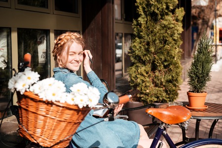 Cheerful beautiful young woman with bicycle writing in notebook and smiling on the bench outdoorsの写真素材