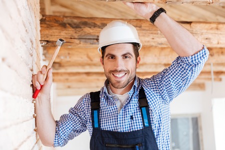 Close-up portrait of cheerful smiling builder using hammer indoorsの写真素材