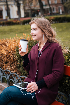 Cheerful attractive young woman drinking coffee and listening to music from tabletの写真素材