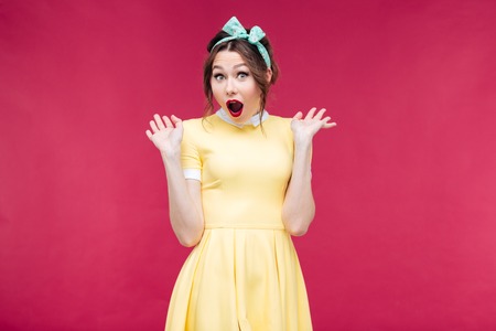 Surprised lovely pinup girl with mouth opened standing over pink background