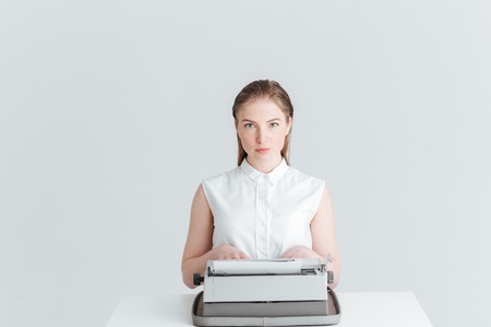 Young woman sitting at the table and typing on retro machine isolated on a white background