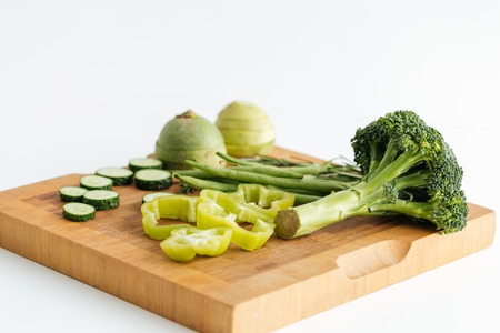 Fresh green vegetables on wooden board over white background