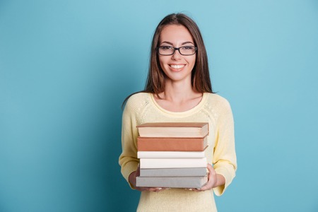 Cute smiling girl holding many books isolated on the blue backgroundの写真素材