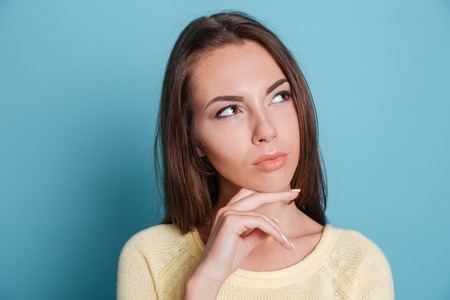 Close-up portrait of a pensive thougtful pretty girl thinking about something isolated on the blue...
