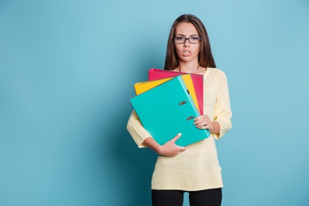 Concentrated young woman holding binders isolated on the blue background