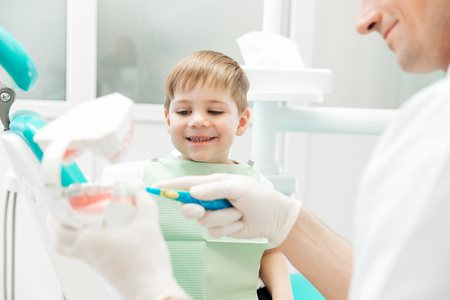 Dentist teaching little boy how to cleaning teeth in dental clinicの写真素材
