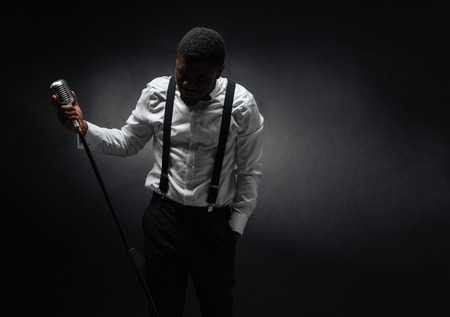 Portrait of afro american male singer posing over dark background