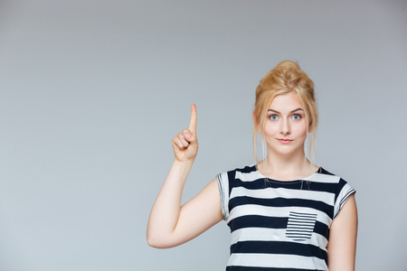 Cute lovely young woman standing and pointing up over white backgroundの写真素材