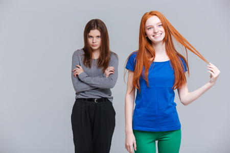 Two smiling redhead and upset brunette young women standing over white backgroundの写真素材