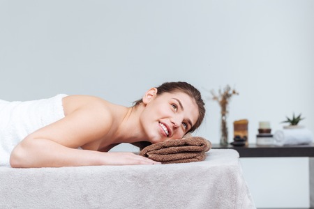 Happy pretty young woman smiling and lying on massage table in spa salonの写真素材