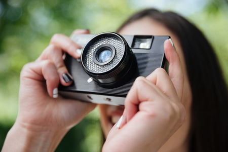 Close-up portrait of a girl taking picture with photo camera outdoors