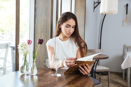 Beautiful young woman in a restaurant with the menu in her handsの写真素材