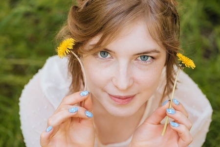 Happy cute young woman with two yellow dandelions outdoorsの写真素材