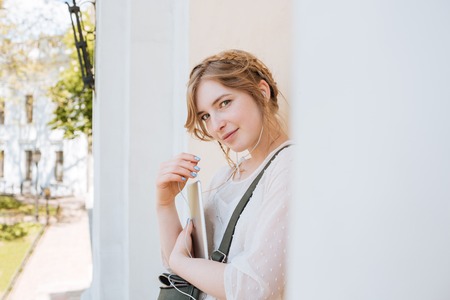 Happy beautiful young woman standing and listening to music from tablet outdoors